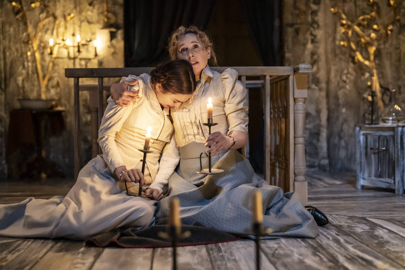 Ruby Thompson as Irina and Michelle Terry as Olga in Three Sisters. Photographed by Johan Persson. Ruby Thompson as Irina and Michelle Terry as Olga in Three Sisters. They are sat down on the floor of the stage. Irina looks as though she might be crying. Olga looks to the ceiling clutching a lit candle with one hand, the other arm draped around Irina's shoulders for comfort.
