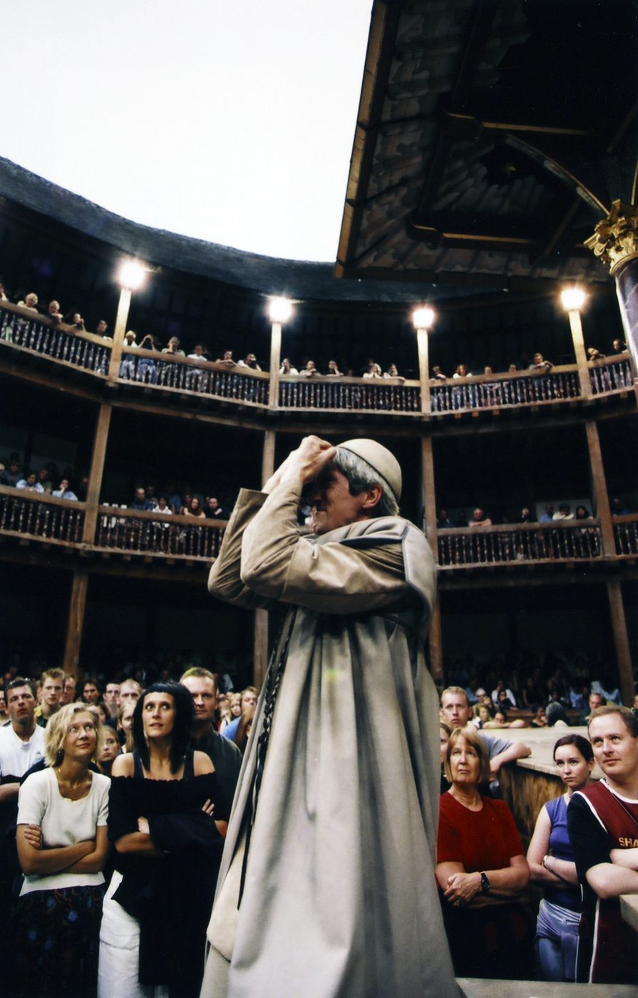 Actor Audience Antony and Cleopatra Shakespeare's Globe A man holding his hands up to his face stands in the Yard of the Globe Theatre, surrounded by audience members.