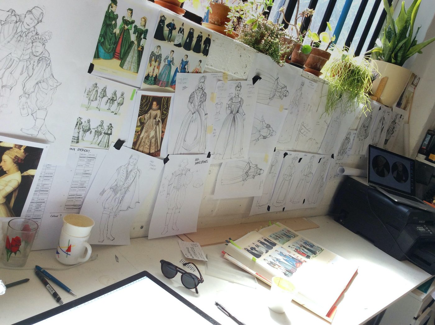 Emilia Costume Sketches Costume Design Jo Scotcher Shakespeare’s Globe A photo of a designer’s desk shows sketches, a sketch book, a mug, a glass and pens