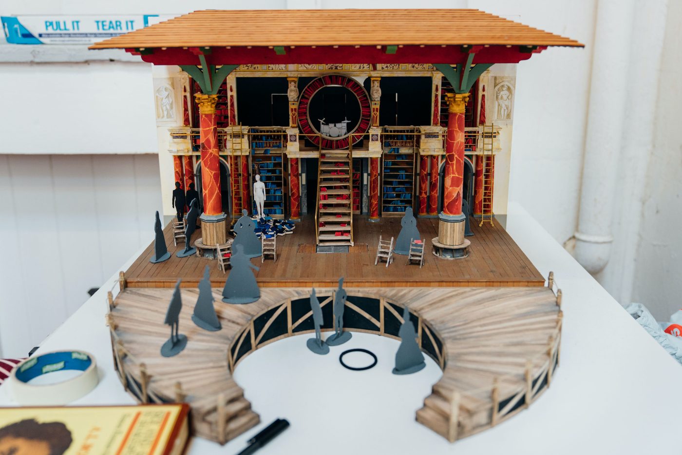 Emilia Model Box Costume Design Jo Scotcher Shakespeare’s Globe A mini set of a theatre which shows a wooden roof, wooden stage, steps, pillars and cardboard cut-out characters
