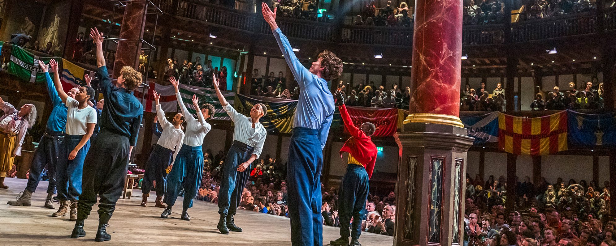 Join and Support Masthead Henry IV Part 1 Shakespeare's Globe 2019 Actors on stage raise their arms to the sky in sync