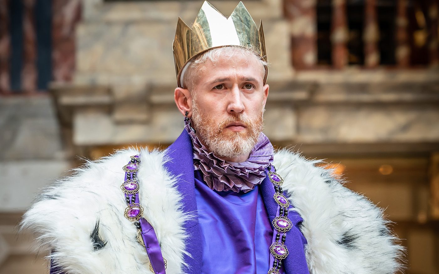 A man wearing a golden crown and a purple costume stares into the distance.