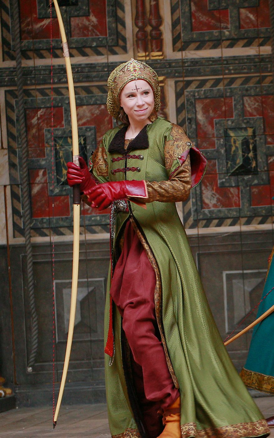 Michelle Terry Hippolyta A Midsummer Night's Dream Shakespeare's Globe An actor wearing a green hunting coat holds a long bow.