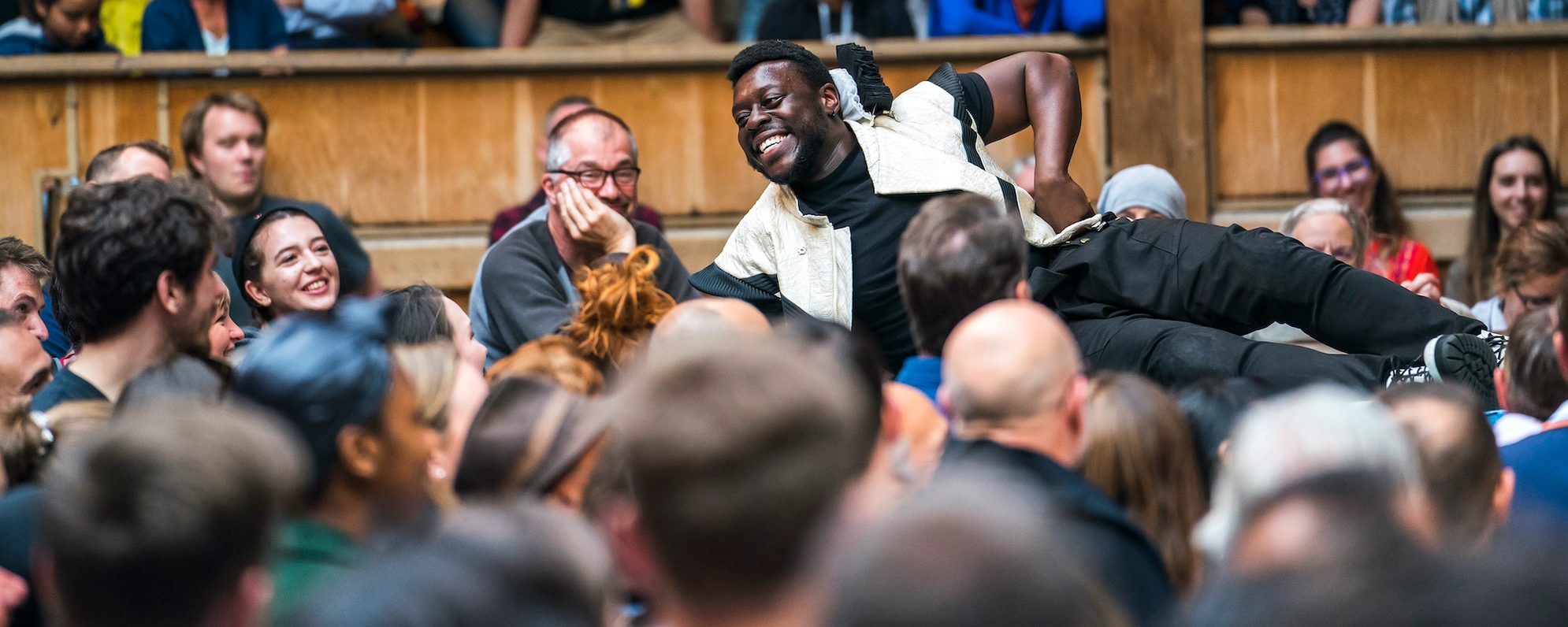 Our Supporters Masthead An actor lies on the edge of a stage performing to the audience