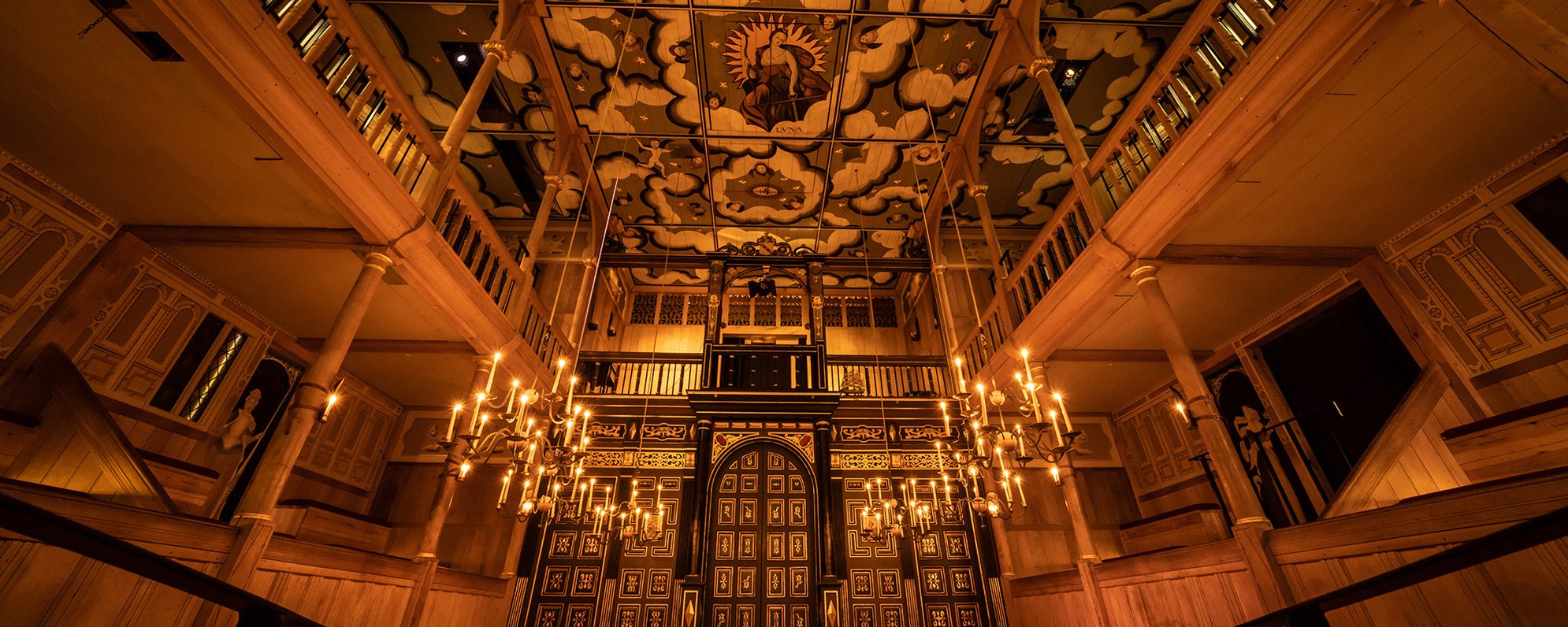 Sam Wanamaker Playhouse 2021 Flush Johan Persson A wide angled shot of the Sam Wanamaker Playhouse with its ornate painting ceiling depicting the Goddess Luna and clouds, hanging candelabra, and panelled painted doors.
