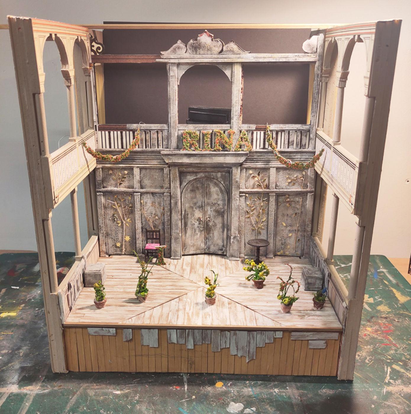 Model box set design of Three Sisters by Oli Townsend. Model box set design of Three Sisters by Oli Townsend. The model shows a relatively bare set. The walls and floor of the stage have been clad in silver birch, and on the back wall there are four silver birch trees depicted, with gold leaves. A floral arrangement spells out
